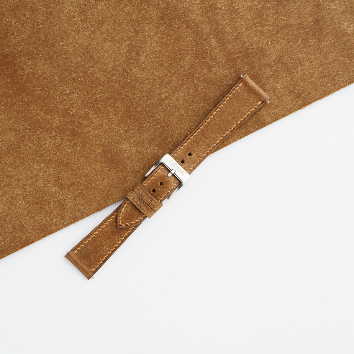 Cognac Pueblo slim strap with cream stitching, buckled and laid across a sheet of brushed Pueblo leather