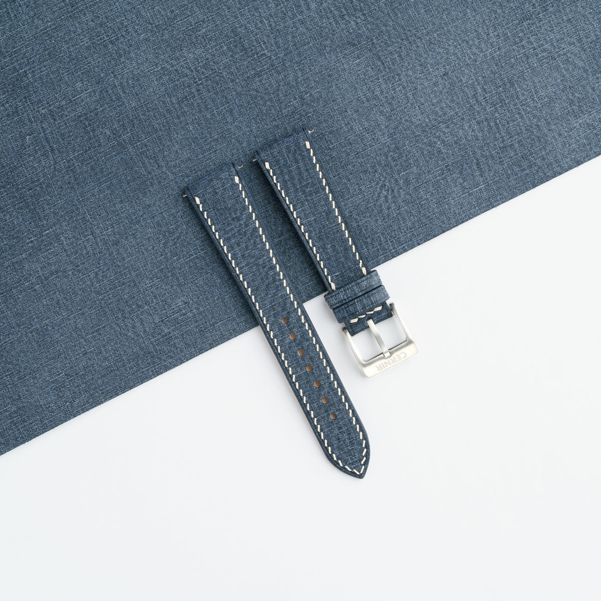 Denim blue Babele slim watch strap laid on a sheet of matching denim blue leather