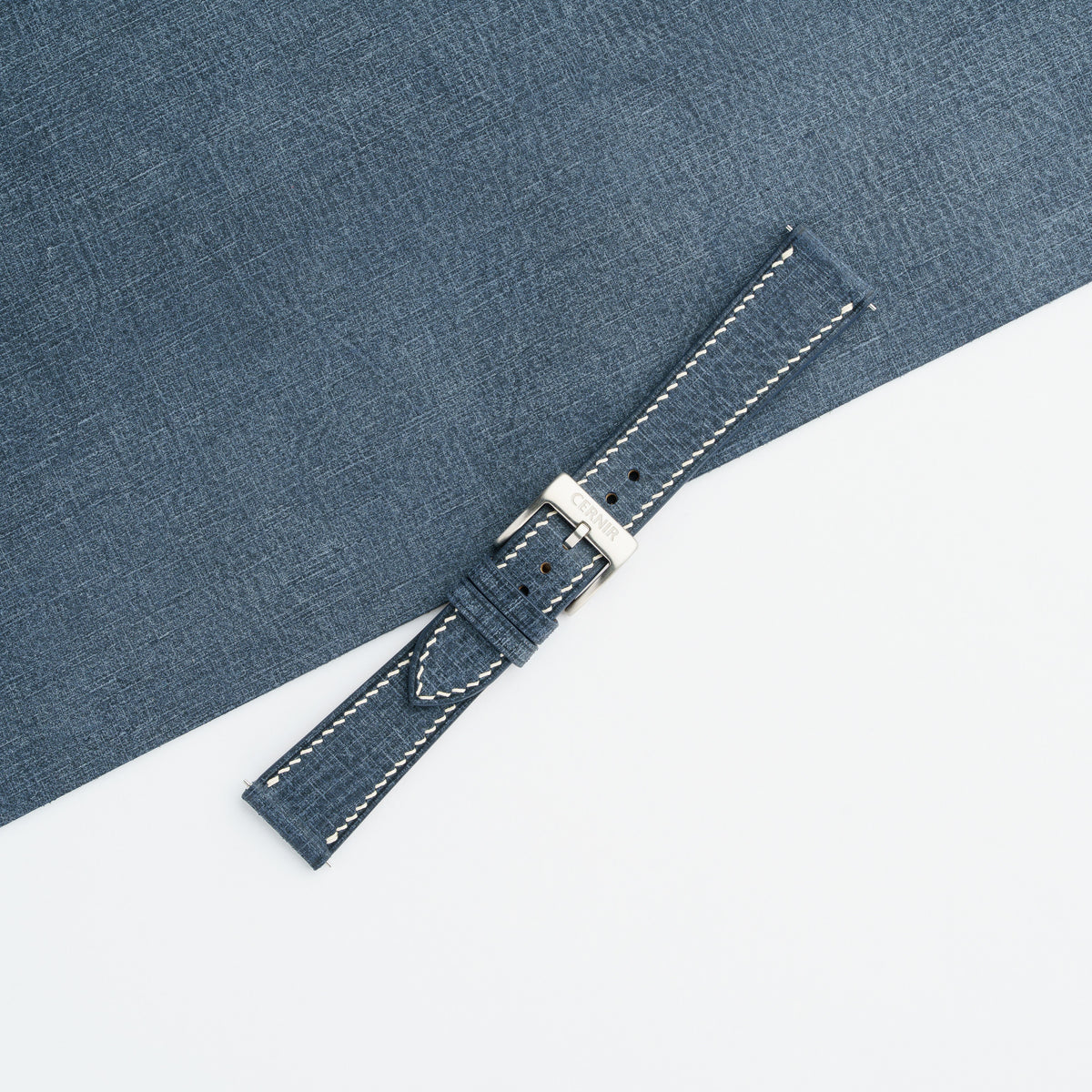 Denim blue Babele slim watch strap fastened with a steel buckle, showing the crosshatched texture