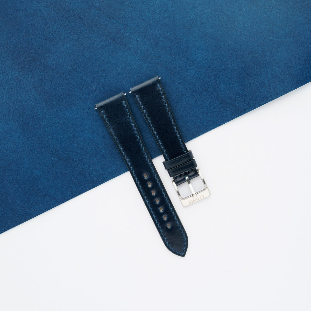 Deep navy shell cordovan slim watch strap laid across a blue leather sheet and white background