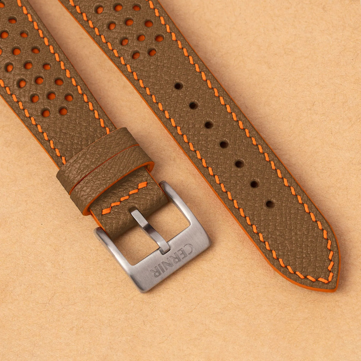 Close-up of round perforations over orange leather, the camel Epsom grain and a silver Cernir buckle
