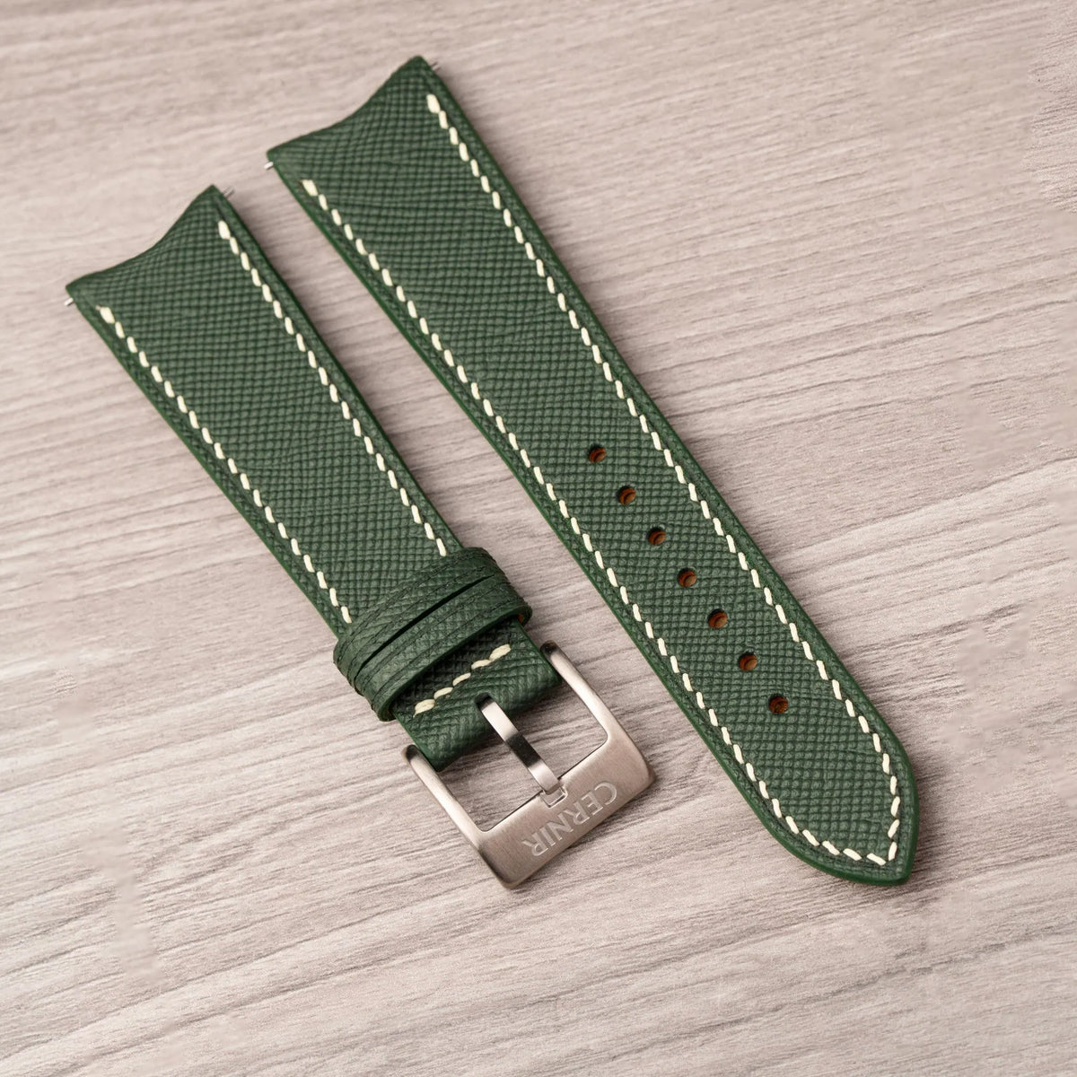Forest Green Saffiano curved end strap with cream stitching and a steel pin buckle on a wooden surface