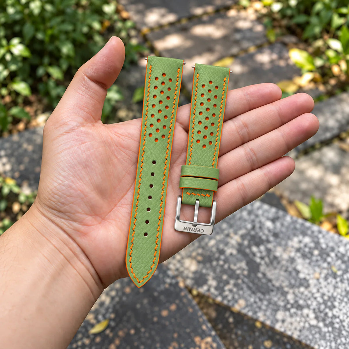 Pistachio Green Epsom Racing Rally strap with orange stitching held in the hand, with a silver Cernir buckle