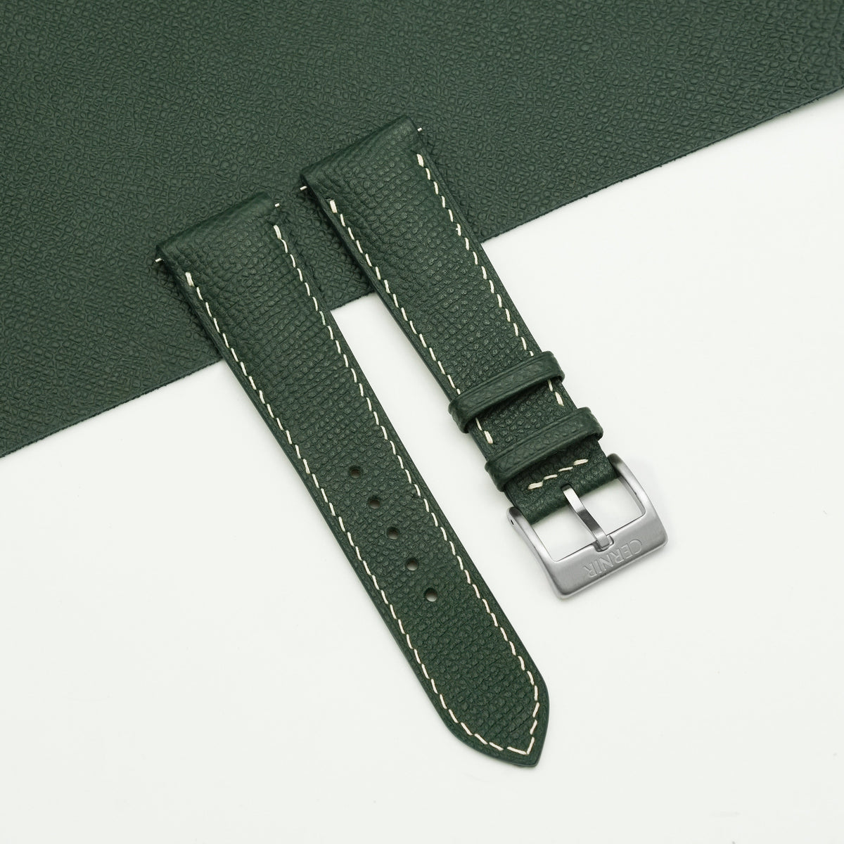Olive green Epsom padded watch strap with cream stitching, showing its raised centre beside a sheet of green leather