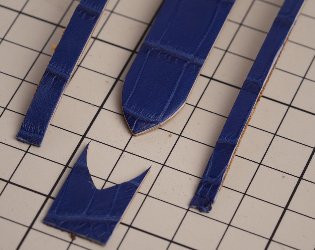 Navy leather strap pieces cut to their final shape on a cutting mat in the Cernir workshop.