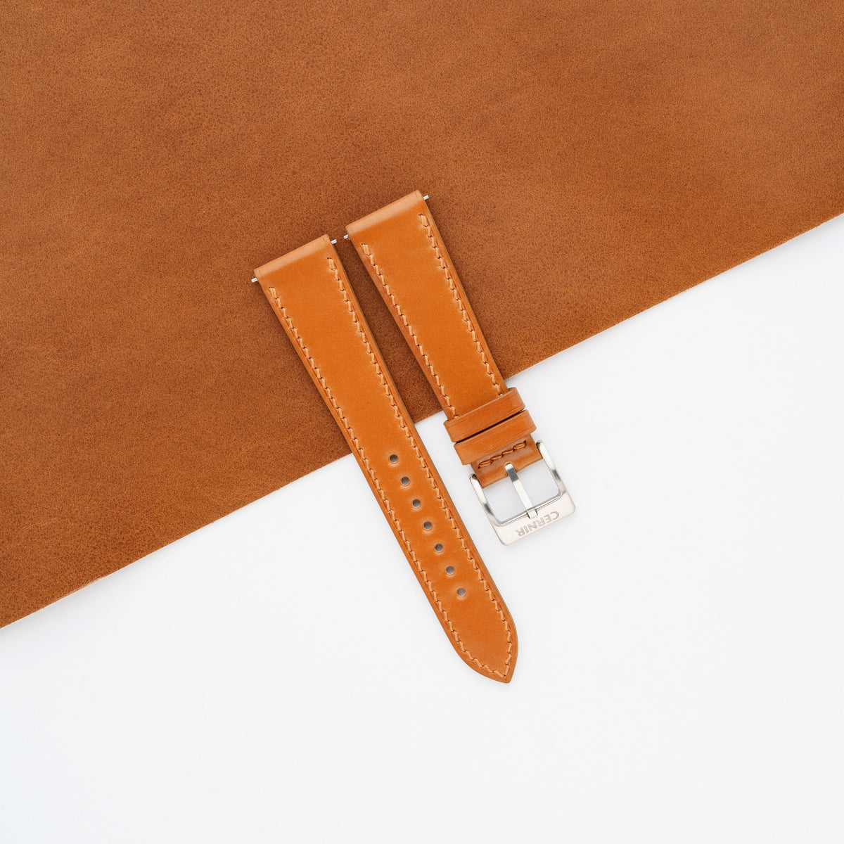 Cognac shell cordovan slim watch strap laid on a sheet of matching cognac leather