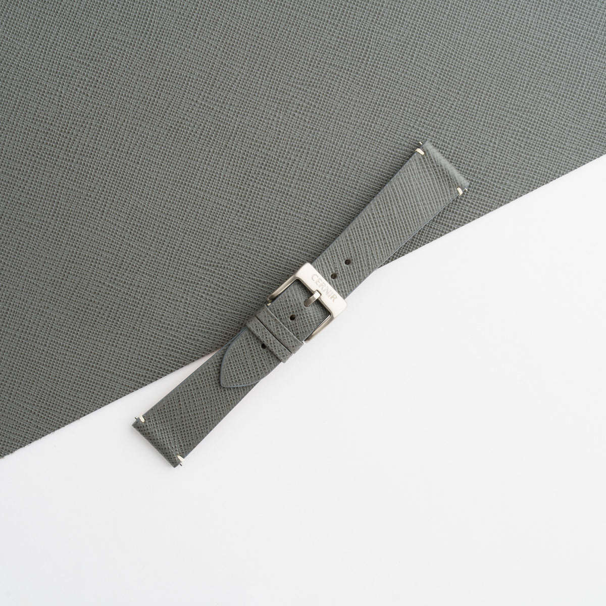 Grey Saffiano side-stitch strap buckled, showing the fine crosshatch grain and clean edges