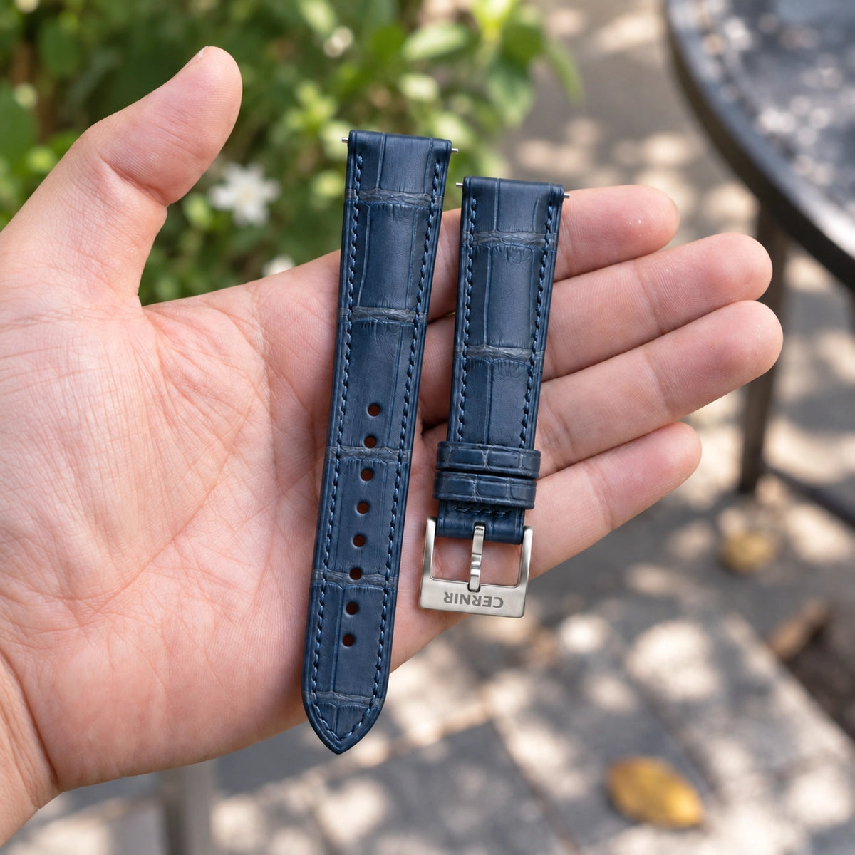 Navy alligator padded watch strap with a steel Cernir buckle, held in an open hand