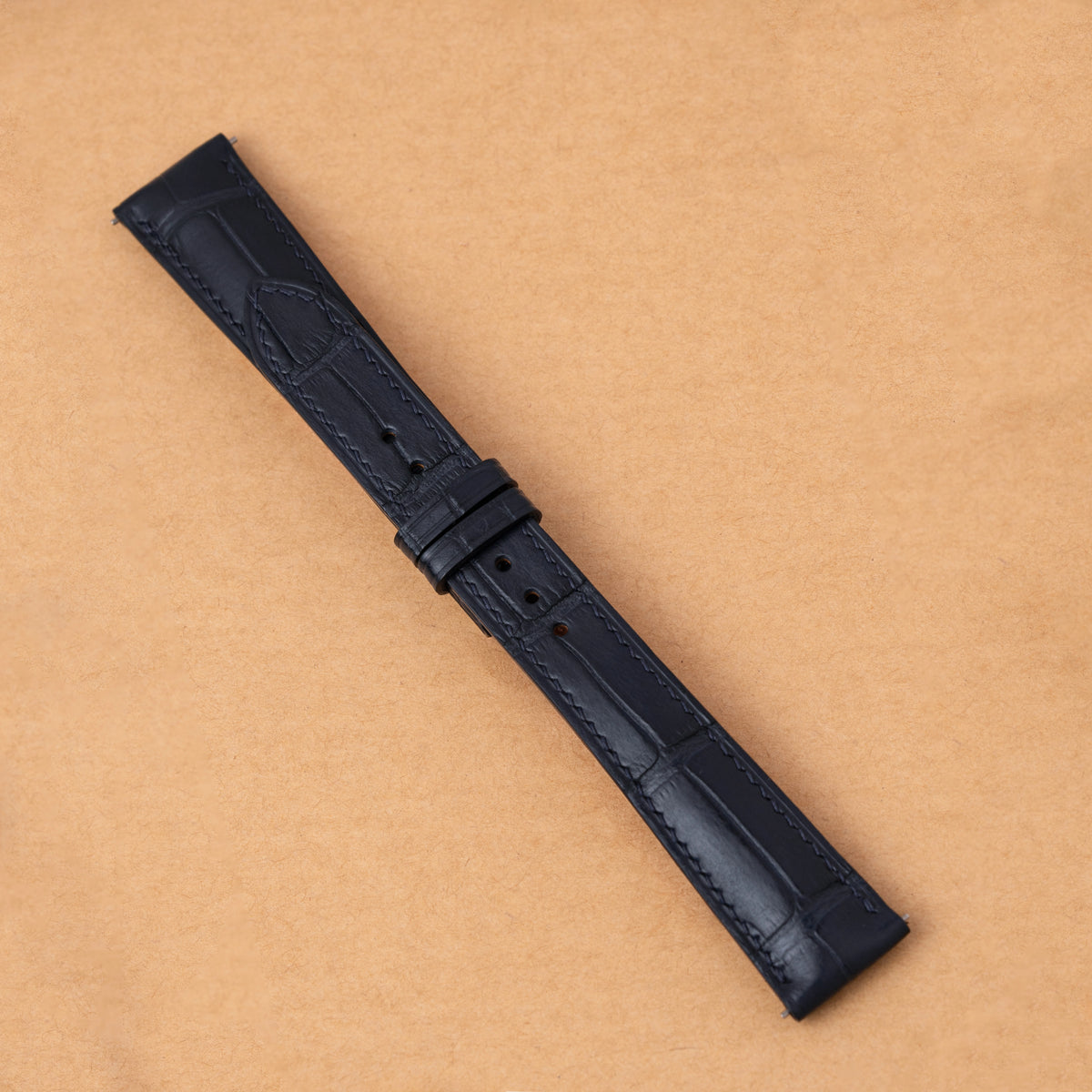 Navy alligator padded watch strap laid flat with its keepers on tan paper
