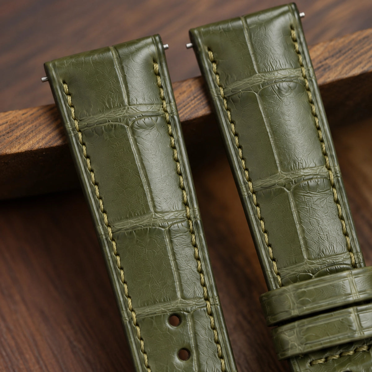 Close-up of the olive green alligator padded strap on wood, showing scales and stitching