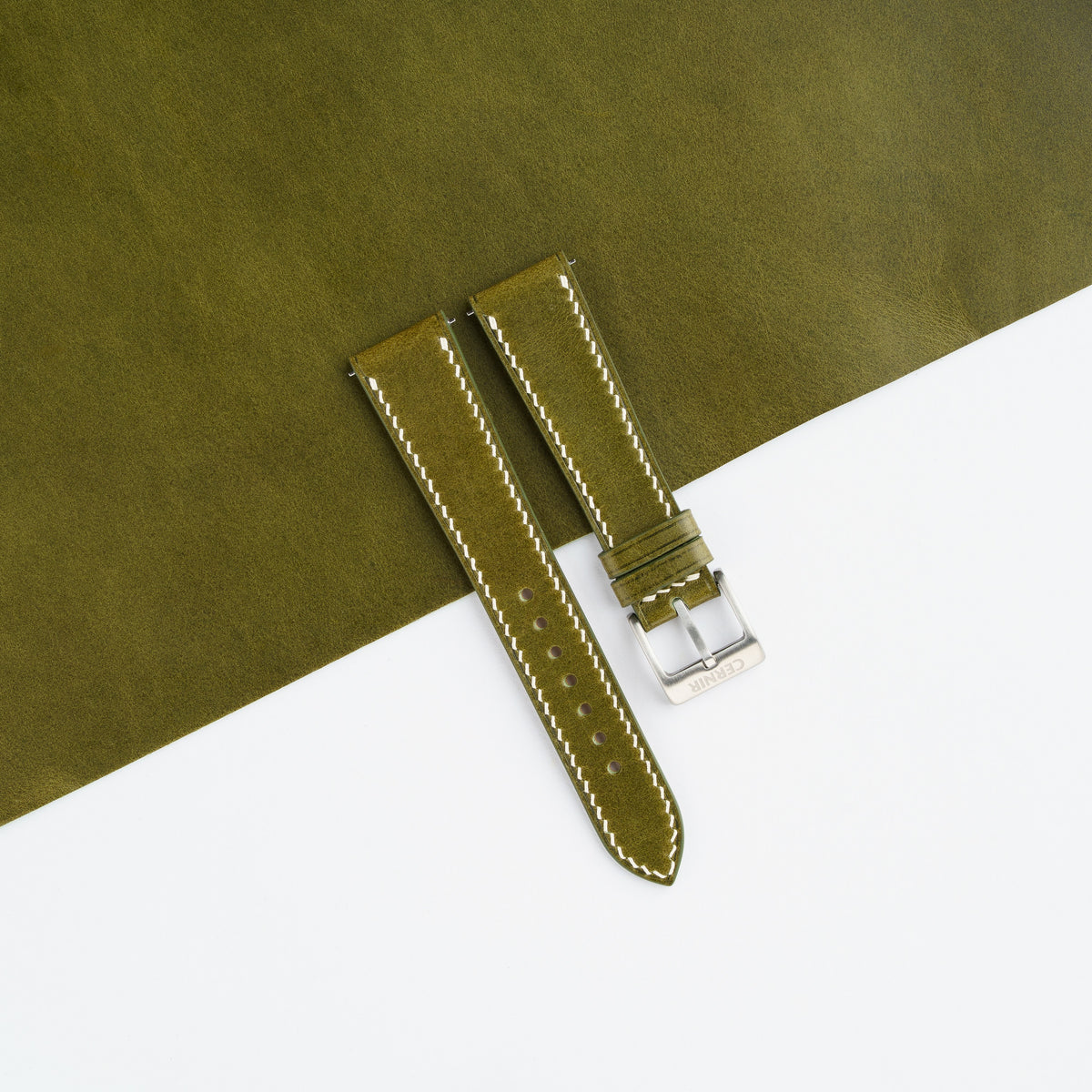 Olive green Buttero slim watch strap laid on a sheet of matching olive leather