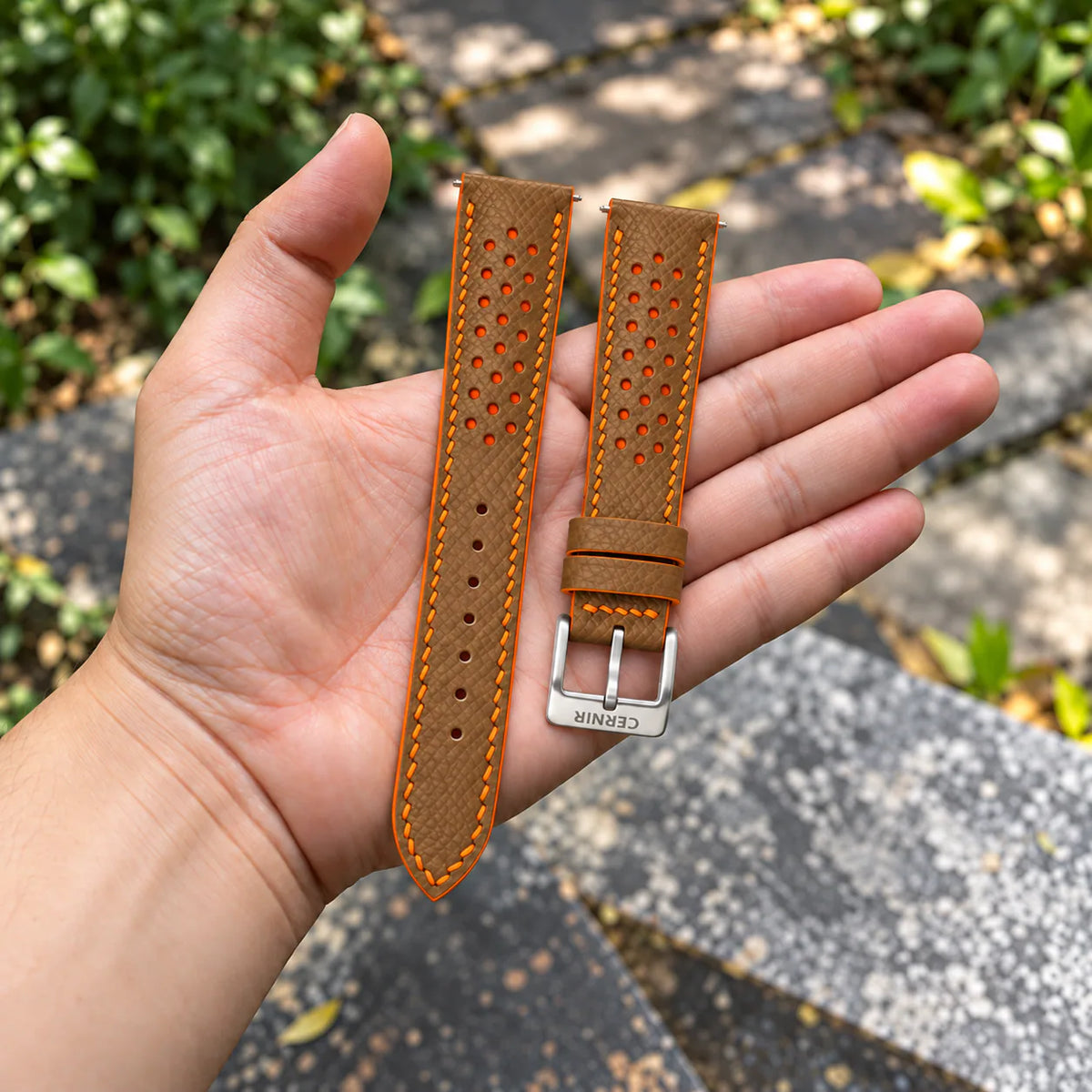 Camel Epsom Racing Rally strap with orange stitching held in the hand, with a silver Cernir buckle