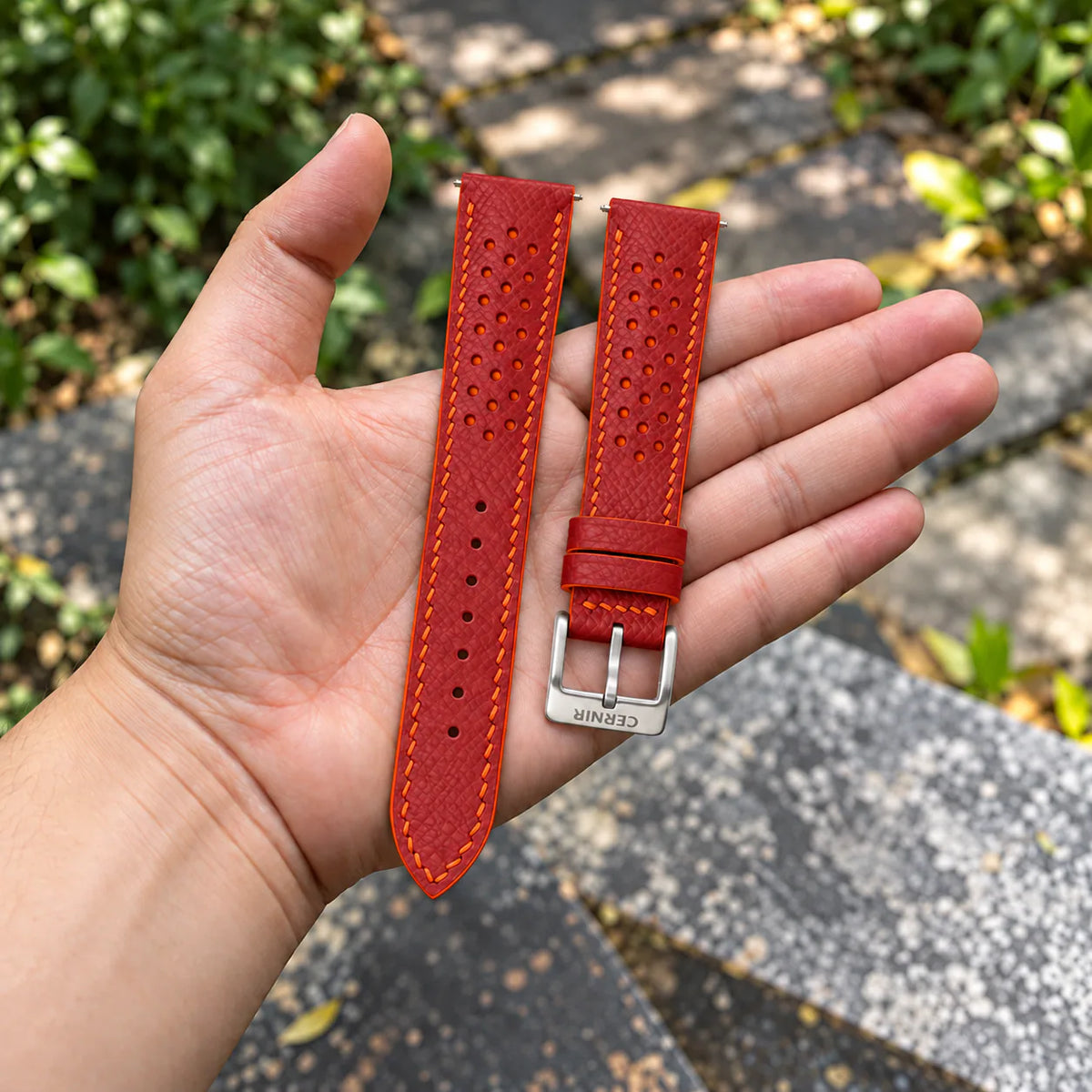 Coral Red Epsom Racing Rally strap with orange stitching held in the hand, with a silver Cernir buckle