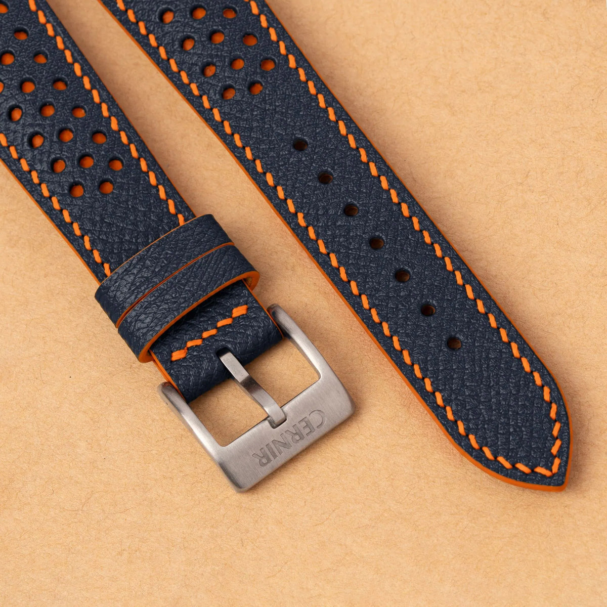 Close-up of round perforations over orange leather, the dark navy Epsom grain and a silver Cernir buckle