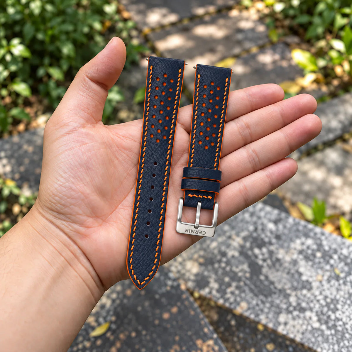Dark Navy Epsom Racing Rally strap with orange stitching held in the hand, with a silver Cernir buckle