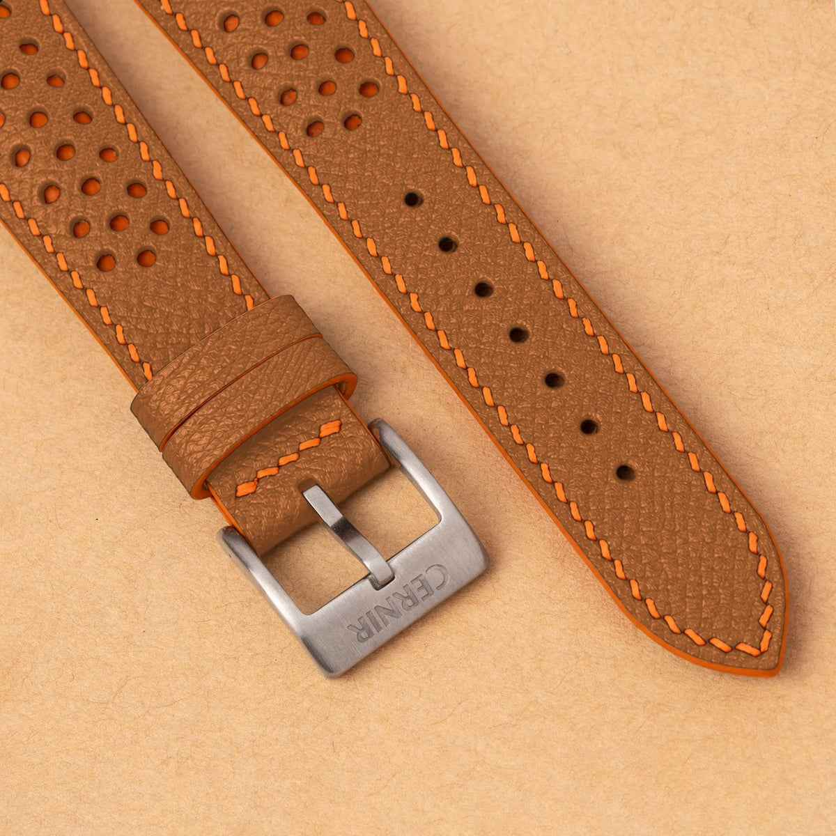 Close-up of round perforations over orange leather, the golden brown Epsom grain and a silver Cernir buckle