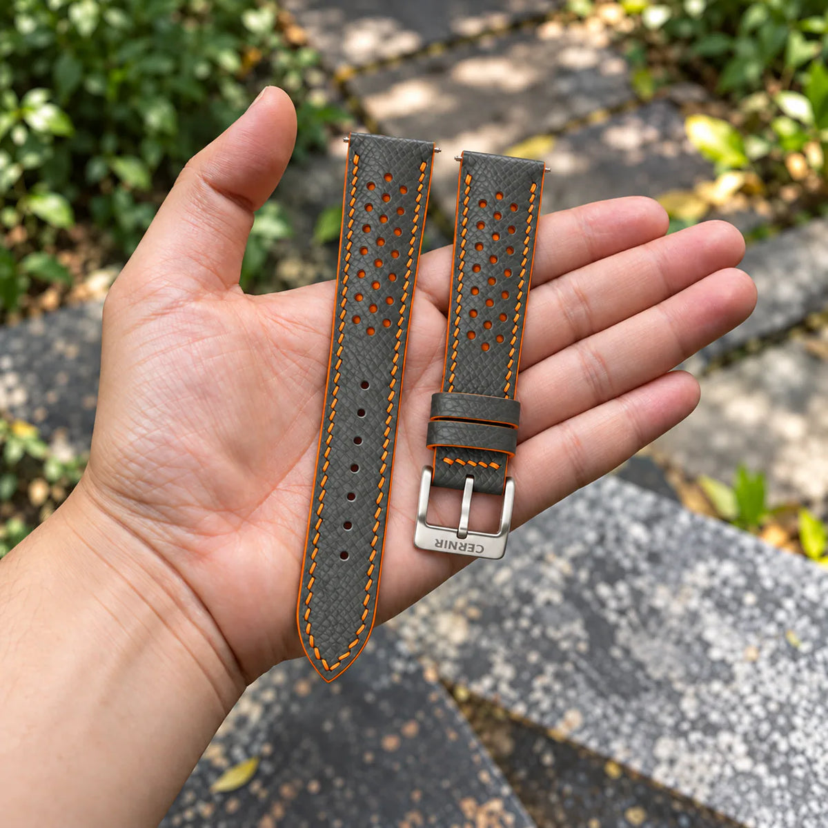 Grey Epsom Racing Rally strap with orange stitching held in the hand, with a silver Cernir buckle