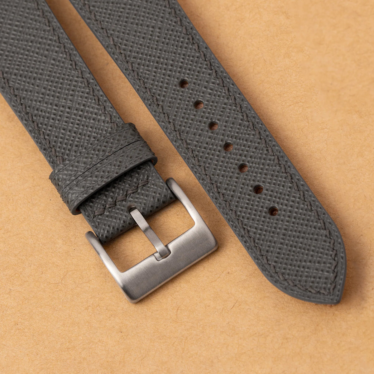 Close-up of the crosshatch Saffiano grain and grey stitching beside the steel buckle of the curved end strap
