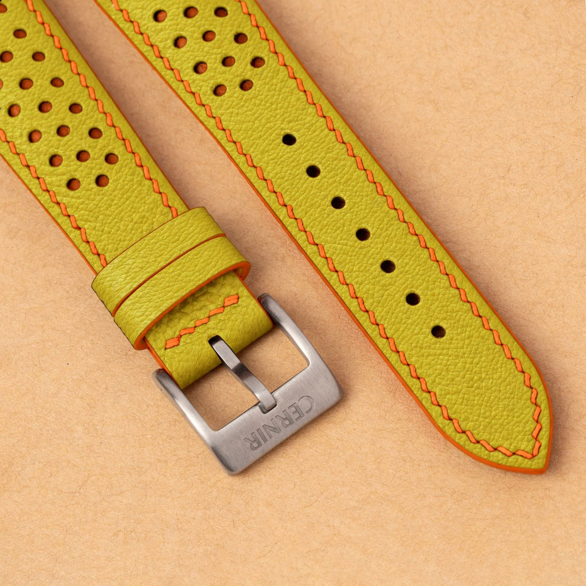 Close-up of round perforations over orange leather, the lemon yellow Epsom grain and a silver Cernir buckle