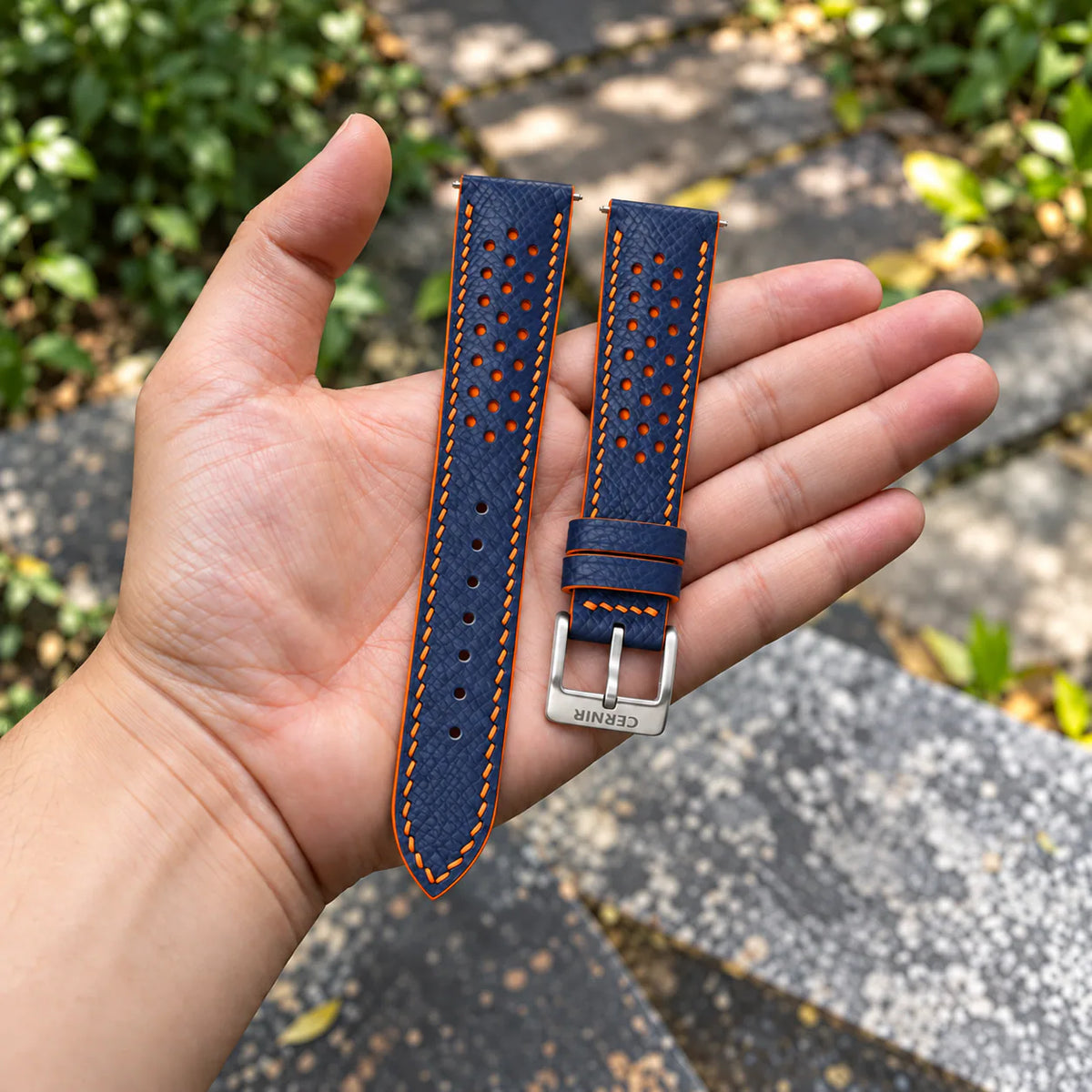 Navy Epsom Racing Rally strap with orange stitching held in the hand, with a silver Cernir buckle
