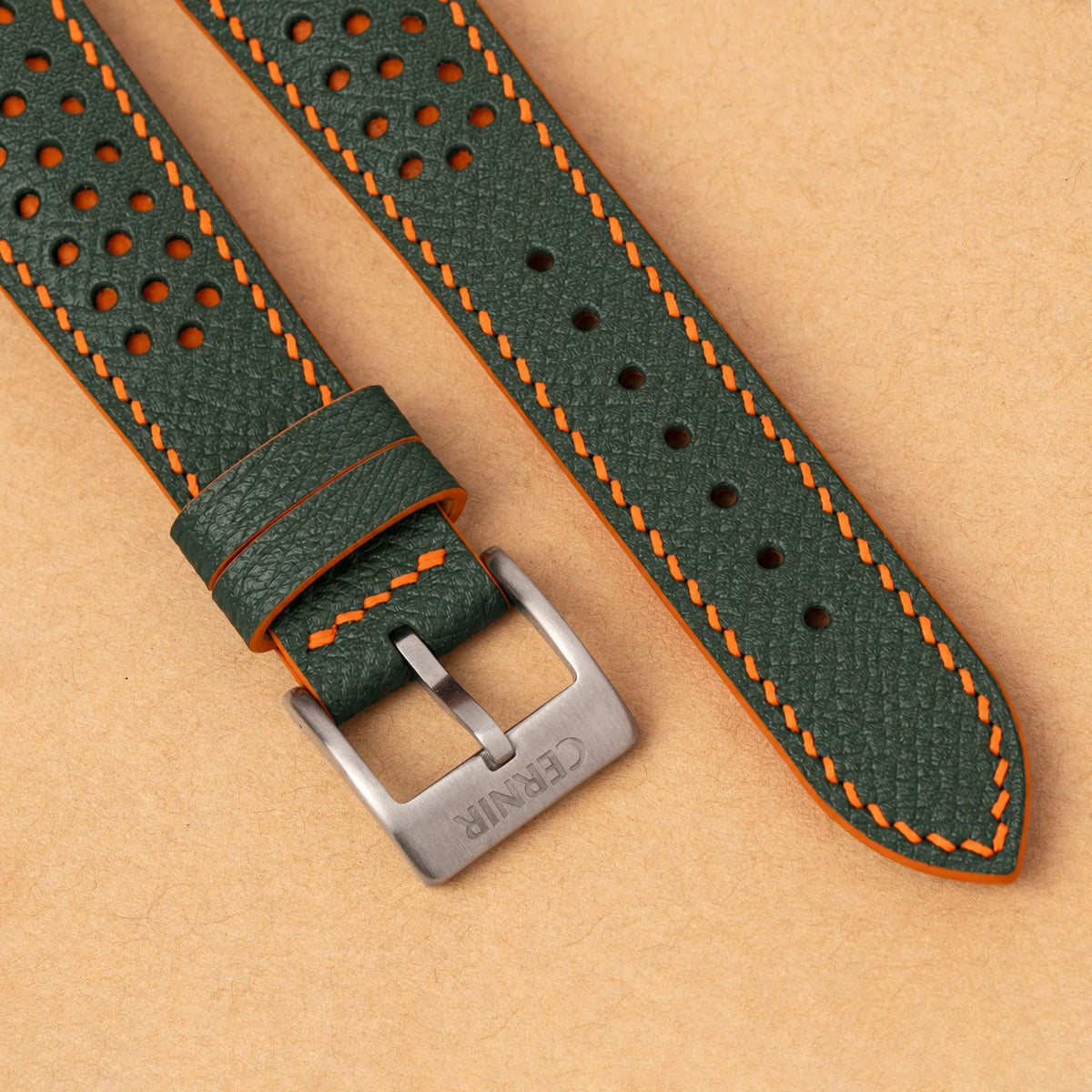 Close-up of round perforations over orange leather, the olive green Epsom grain and a silver Cernir buckle
