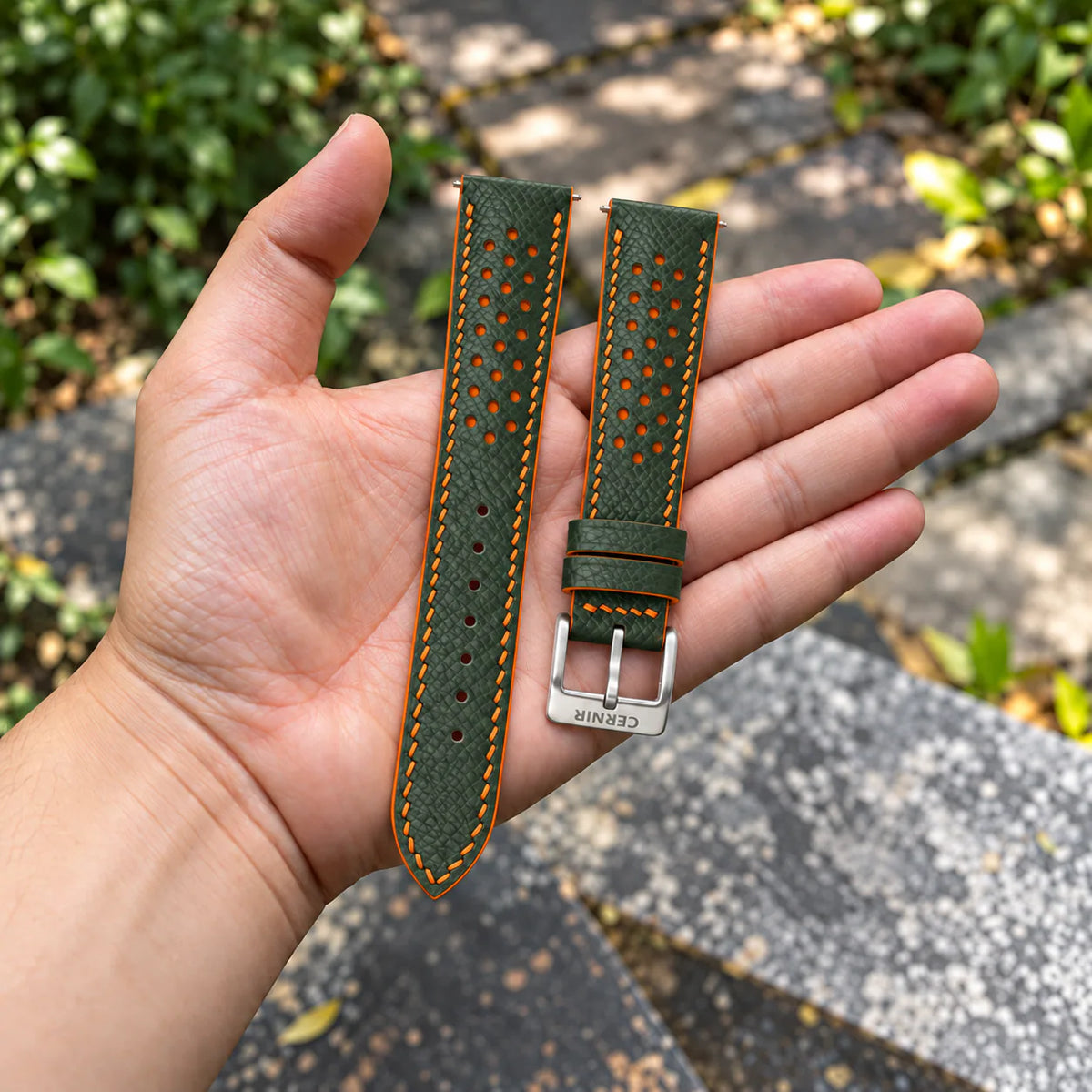 Olive Green Epsom Racing Rally strap with orange stitching held in the hand, with a silver Cernir buckle