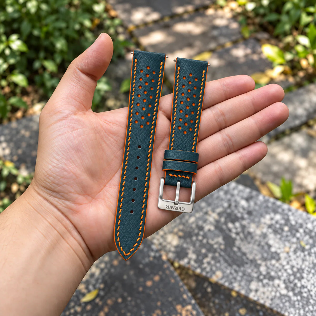 Petrol Blue Epsom Racing Rally strap with orange stitching held in the hand, with a silver Cernir buckle