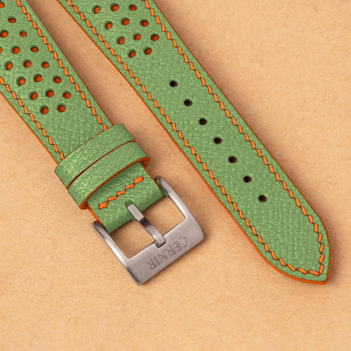 Close-up of round perforations over orange leather, the pistachio green Epsom grain and a silver Cernir buckle
