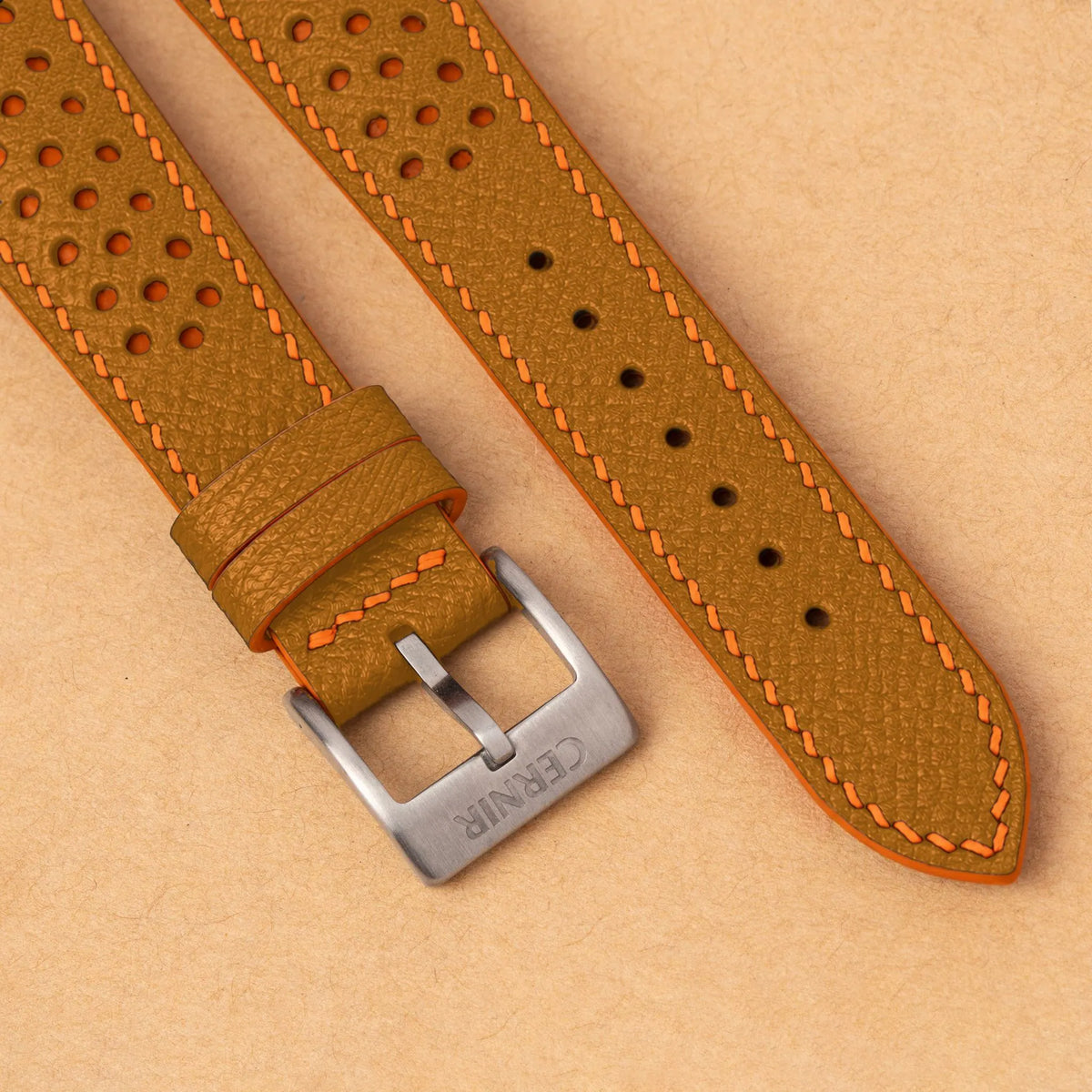Close-up of round perforations over orange leather, the tan Epsom grain and a silver Cernir buckle