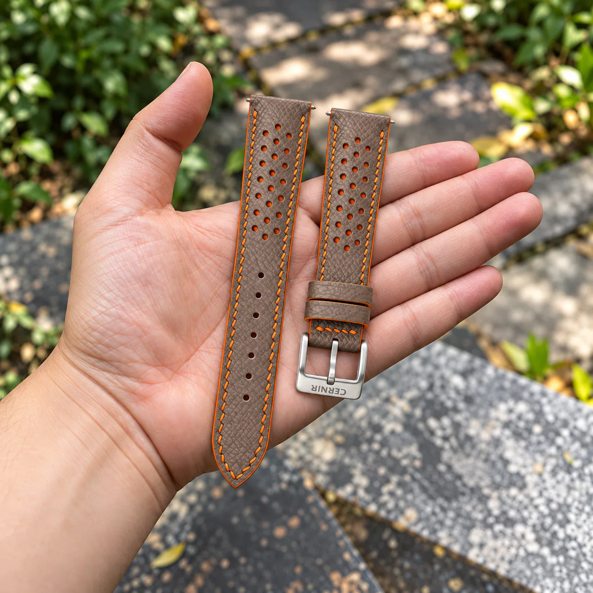 Taupe Epsom Racing Rally strap with orange stitching held in the hand, with a silver Cernir buckle