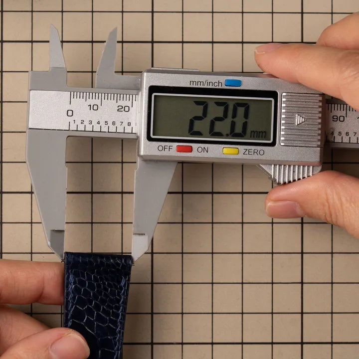 Calipers closed across the very end of a leather strap, the part that sits between the lugs. The display reads 22.0 mm.