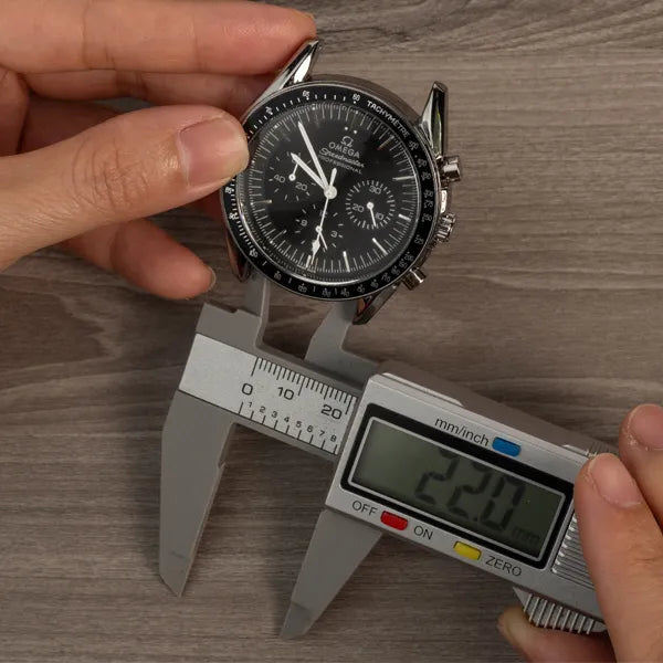 Digital calipers with the small inside jaws placed in the gap between a watch's lugs, touching the inside edge of each lug. The display reads 22.0 mm.